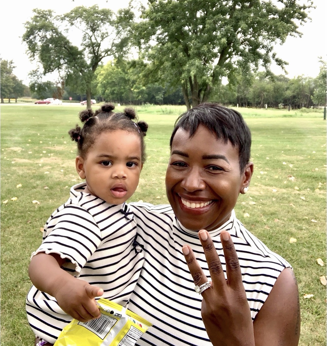 A woman holding a young child outdoors, both wearing matching striped outfits