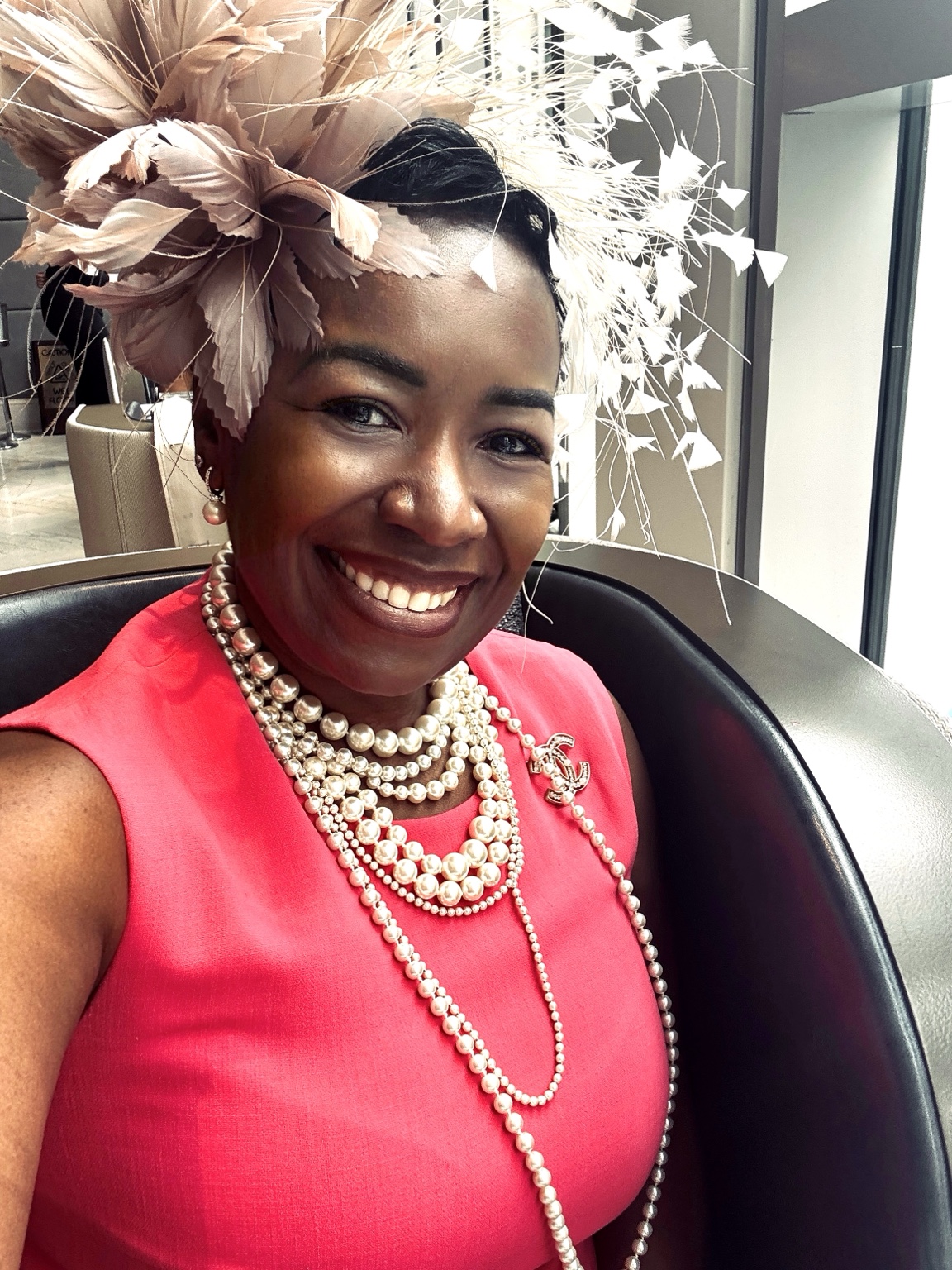 Portrait in a bright pink dress with layered pearls and a feathered fascinator